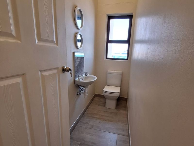 A compact guest bathroom featuring modern tiled flooring, a wall-mounted basin, and a standard toilet.