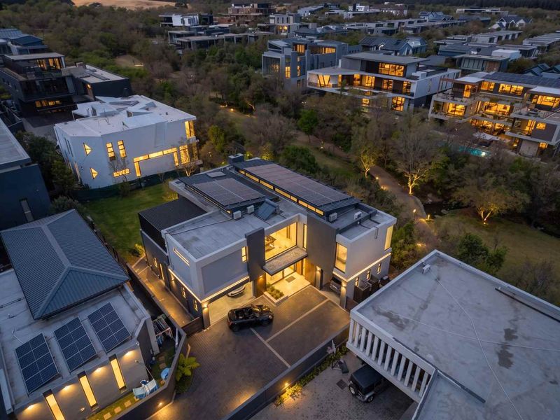 Aerial view of a modern multi-story residential property featuring solar panels, a paved driveway, and integrated garage lighting within a landscaped estate.