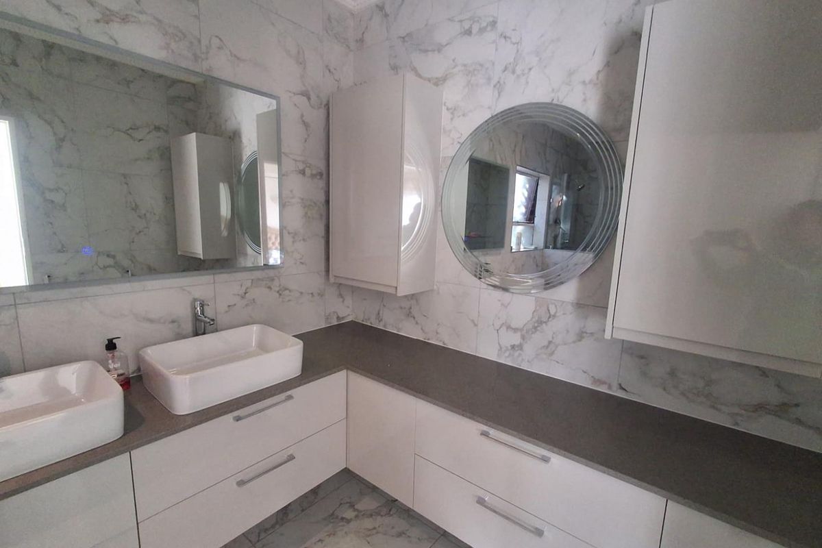 Modern bathroom featuring a double vanity with white vessel sinks, stone-look countertops, marble-effect wall tiles, and integrated cabinetry with dual mirrors.