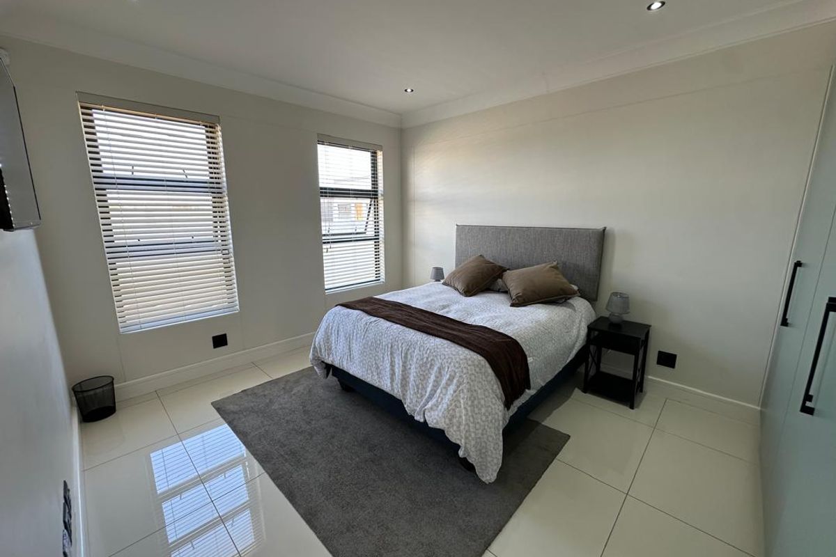 A bright and modern bedroom featuring large windows with fitted blinds, recessed ceiling lighting, and polished floor tiles.