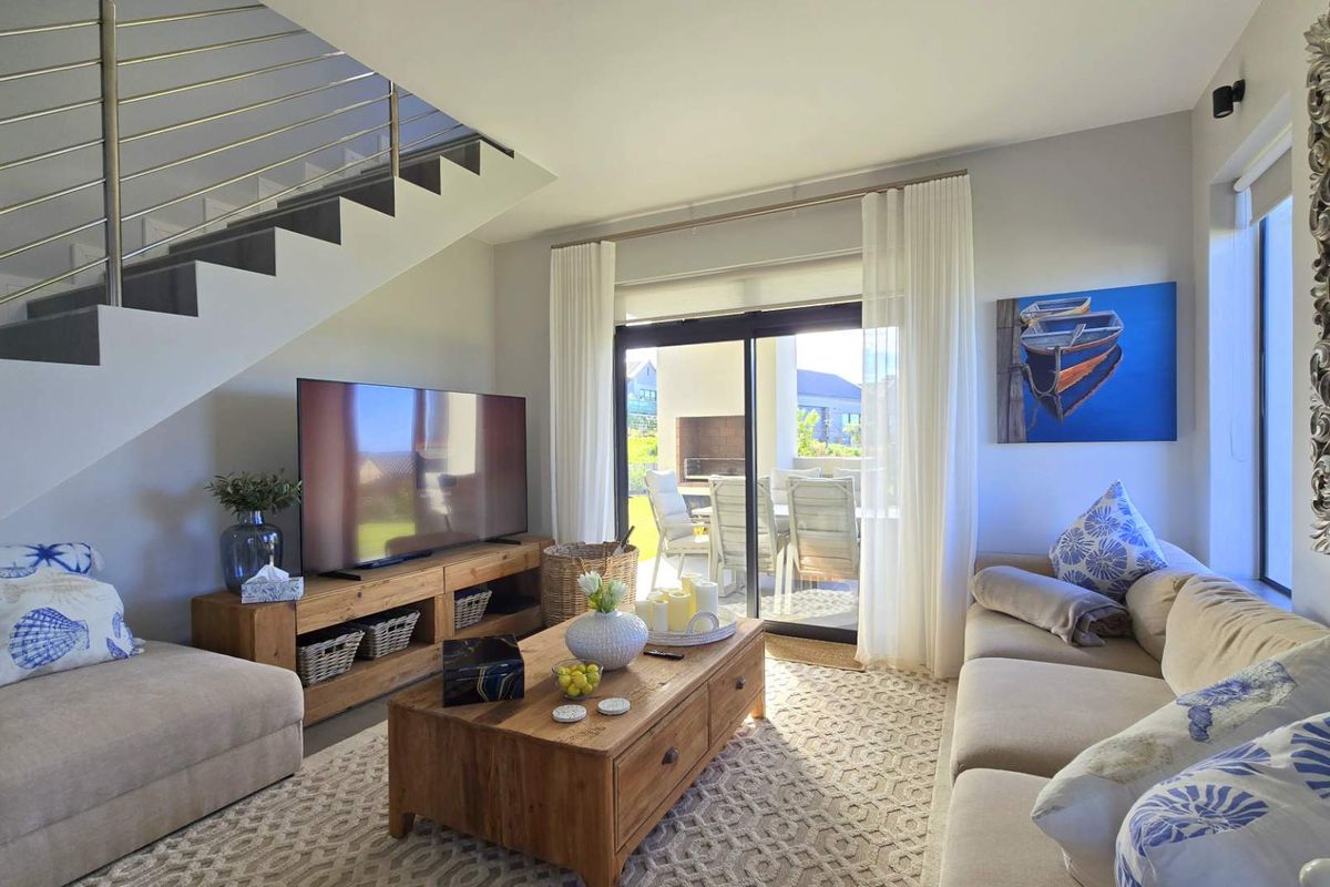 A bright and modern living room featuring a staircase with stainless steel railings, large sliding glass doors leading to a patio, and neutral finishes.