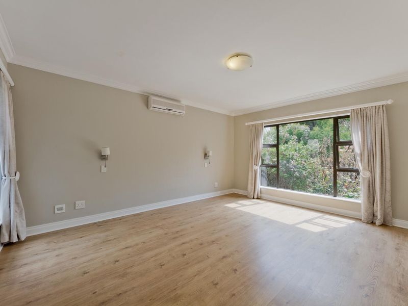 A bright and spacious bedroom featuring light wood-look laminate flooring, an air conditioning unit, and large windows with garden views.