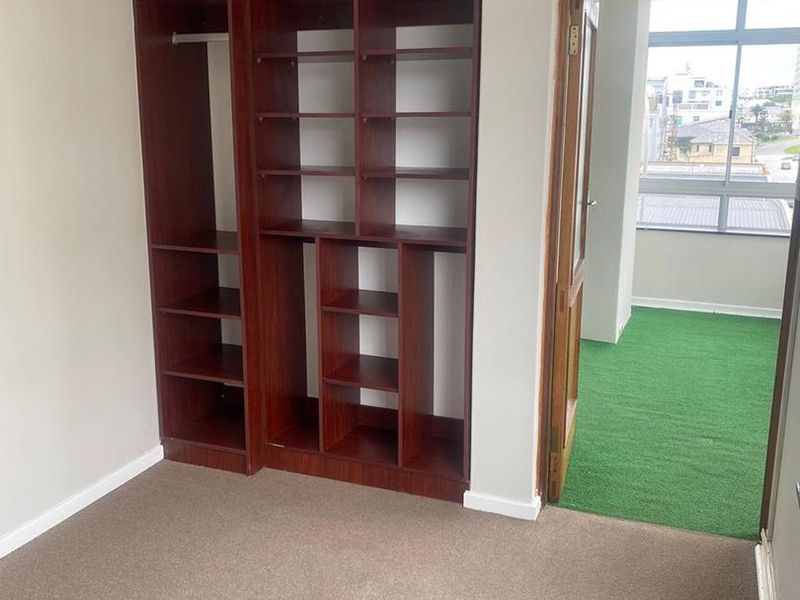 A bedroom featuring built-in wooden shelving and wardrobe storage, with carpeted flooring and direct access to an adjacent balcony area.