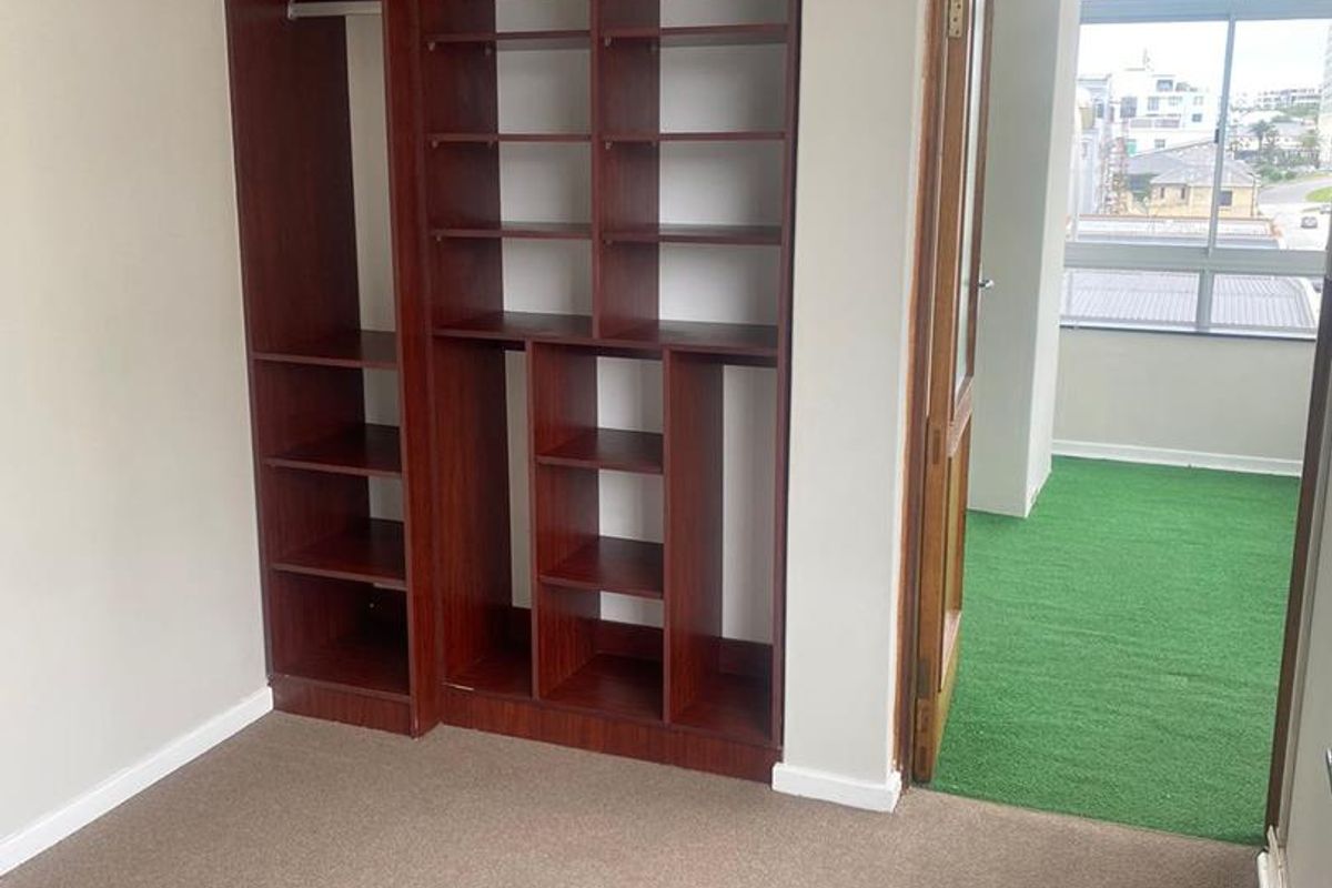 A bedroom featuring built-in wooden shelving and wardrobe storage, with carpeted flooring and direct access to an adjacent balcony area.