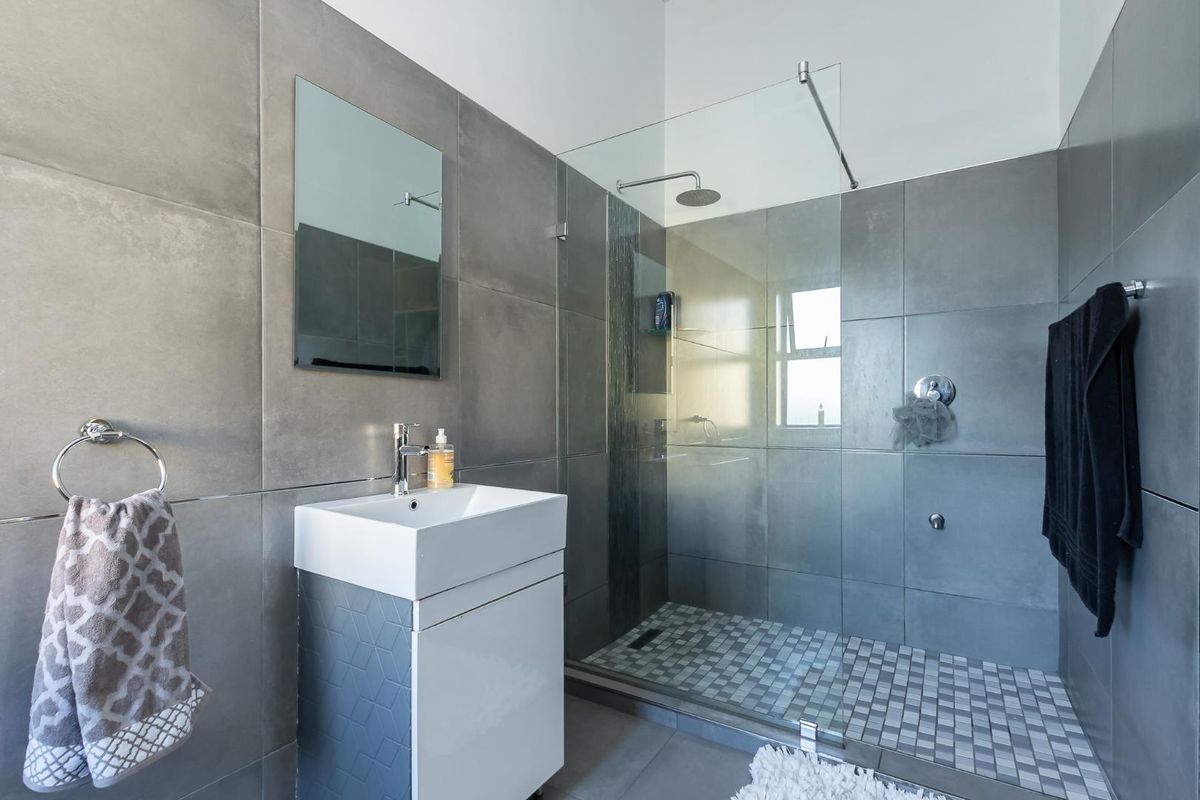 Modern bathroom featuring a walk-in shower with a glass screen, rain shower head, vanity basin, and contemporary large-format grey wall tiling.