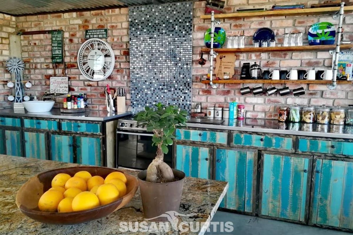 Rustic kitchen area featuring exposed brick walls, industrial-style shelving, stainless steel countertops, and custom distressed blue cabinetry.
