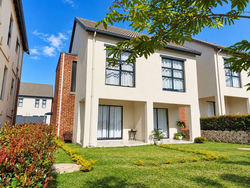 Rear view of a modern two-story townhouse featuring a covered patio, sliding glass doors, and a well-maintained private garden.