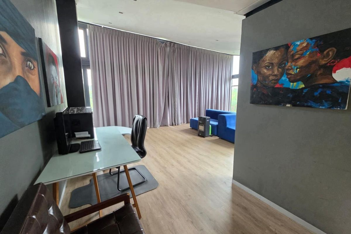 A spacious room featuring modern wood-look flooring, recessed ceiling lighting, and floor-to-ceiling curtains covering large windows.