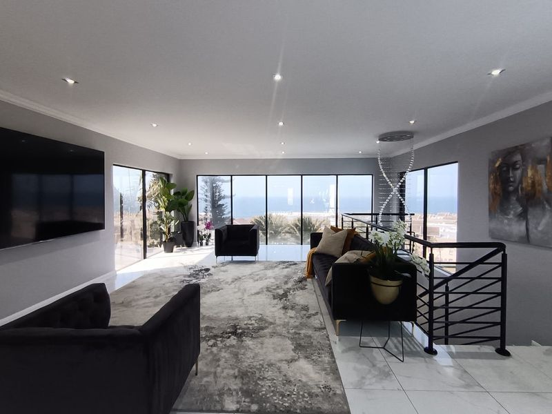 Spacious modern living area featuring large floor-to-ceiling windows with ocean views, tiled flooring, and recessed lighting.