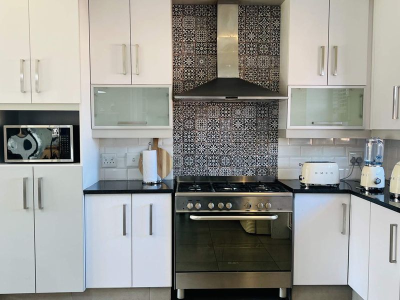 Modern kitchen featuring white cabinetry, stone countertops, a gas stove with a decorative tiled splashback, and integrated microwave.