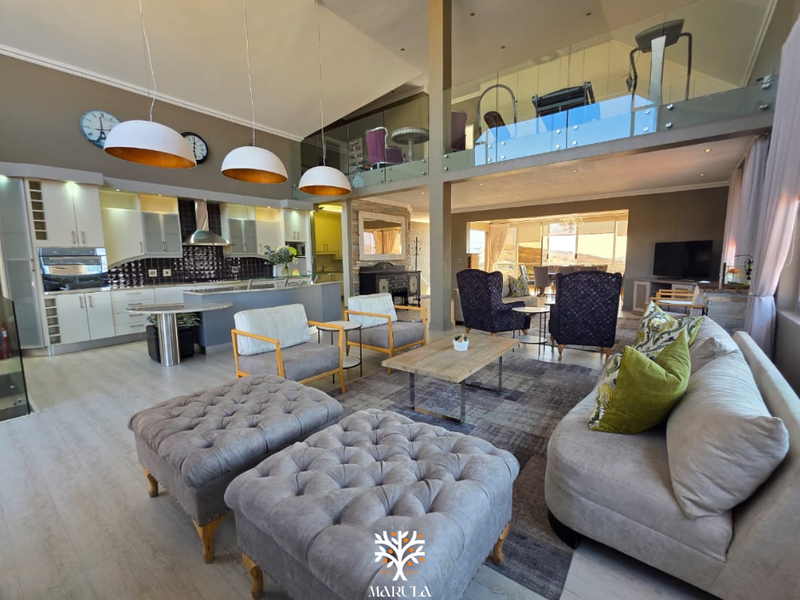 Spacious open-plan living area featuring a modern kitchen, high vaulted ceilings, and a mezzanine level with glass balustrades overlooking the main living space.