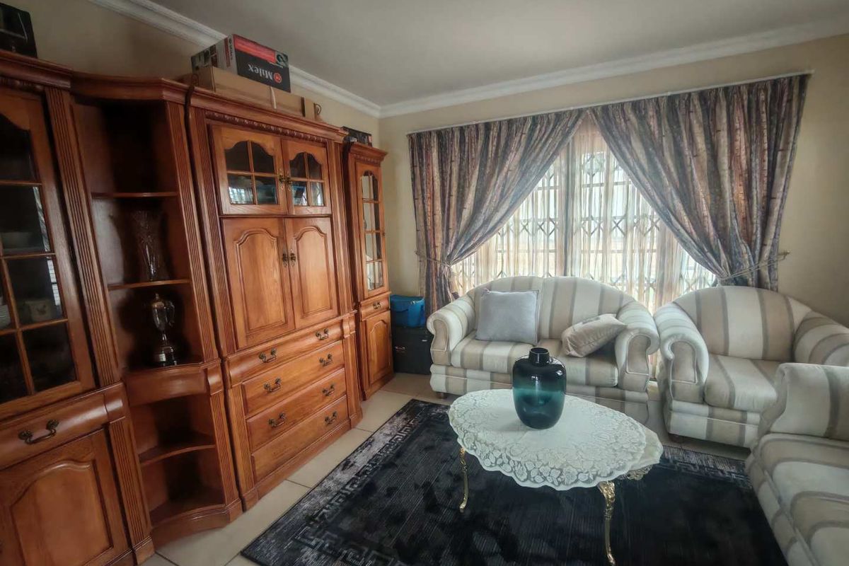 A living room featuring tiled flooring, crown molding, and a large window with security gate.