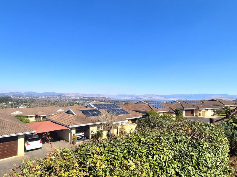 An elevated aerial view of a residential townhouse complex featuring tiled roofs, solar panel installations, and surrounding landscape views.