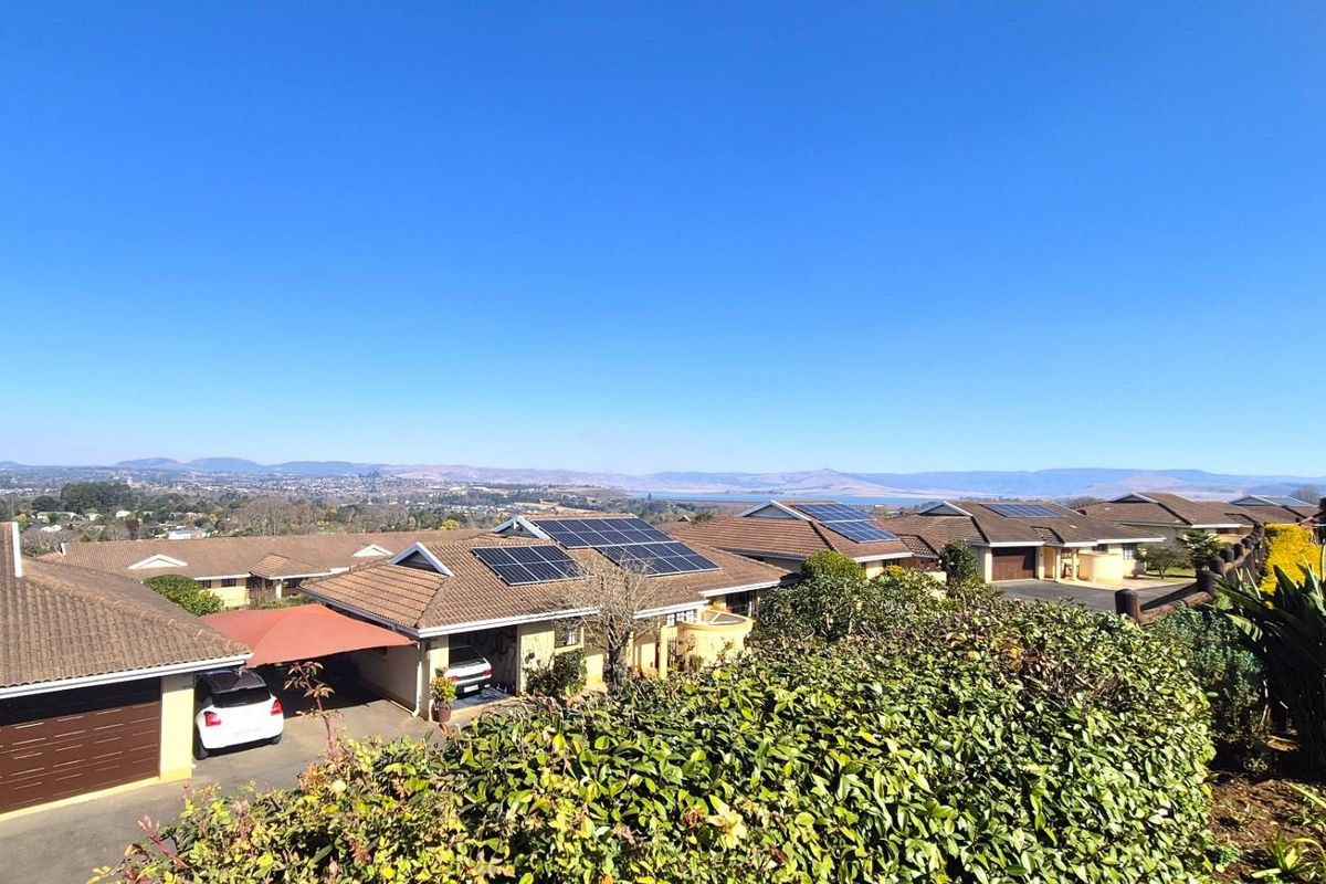 An elevated aerial view of a residential townhouse complex featuring tiled roofs, solar panel installations, and surrounding landscape views.