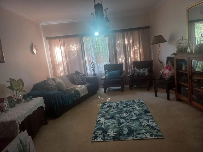 A living room featuring carpeted flooring, coving, and large windows with curtain rails, offering a comfortable and traditional living space.
