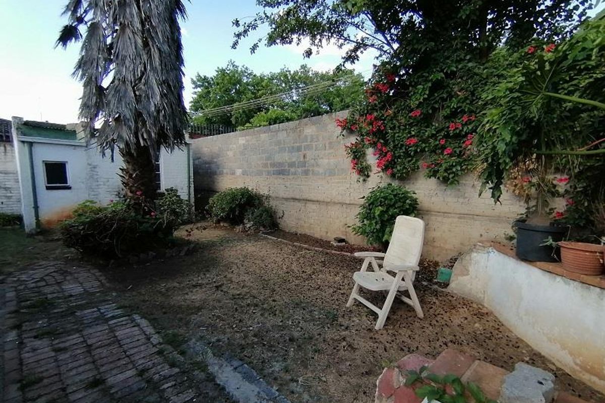 A private rear garden area featuring a brick-paved pathway, established greenery, and a perimeter masonry boundary wall.