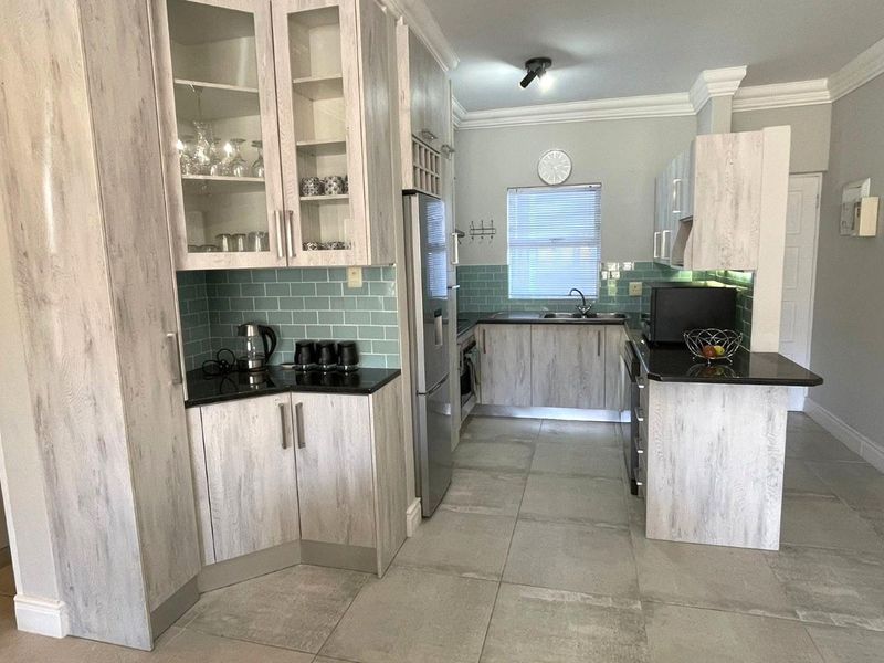 Modern kitchen featuring light wood-grain cabinetry, black granite countertops, a stylish teal subway tile backsplash, and large format floor tiles.