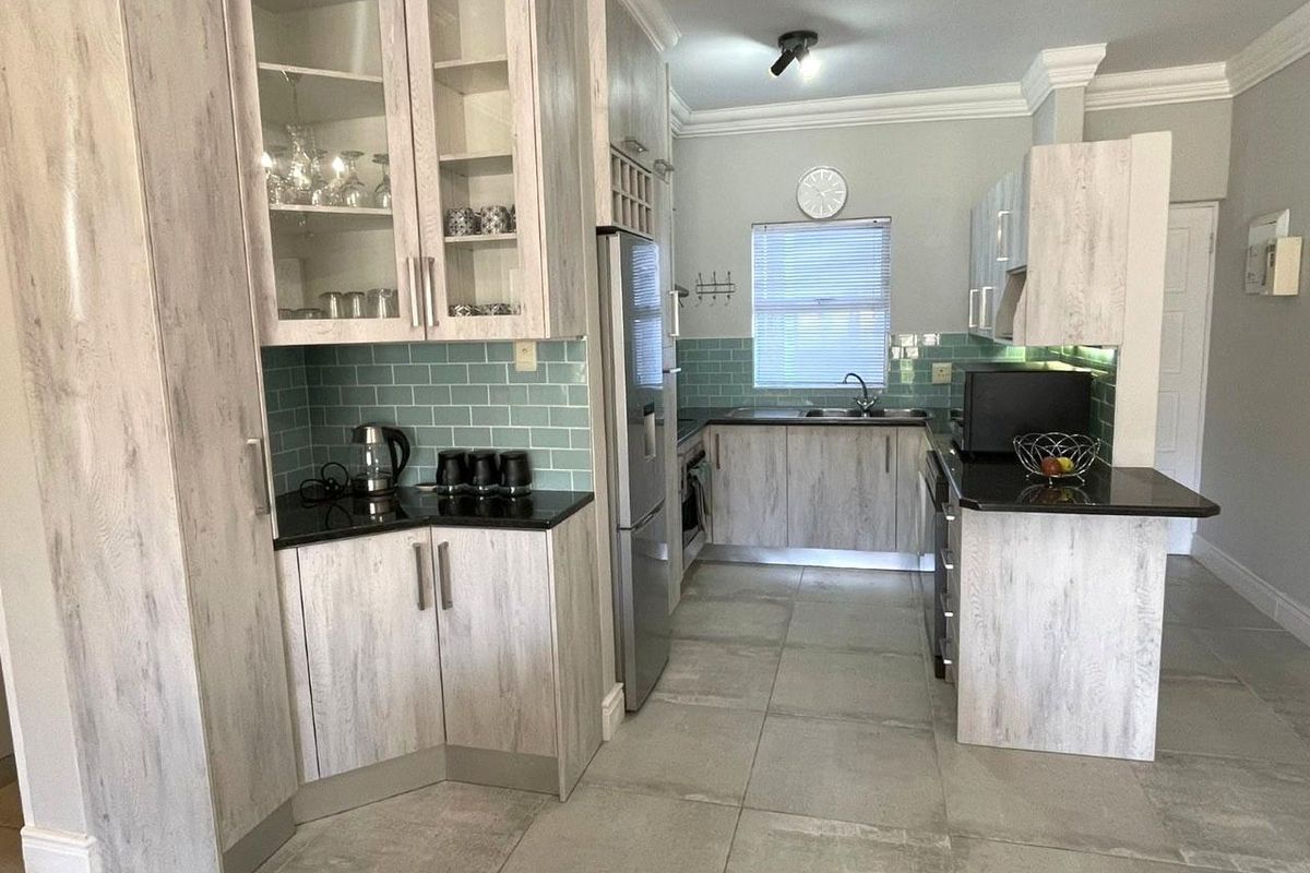 Modern kitchen featuring light wood-grain cabinetry, black granite countertops, a stylish teal subway tile backsplash, and large format floor tiles.