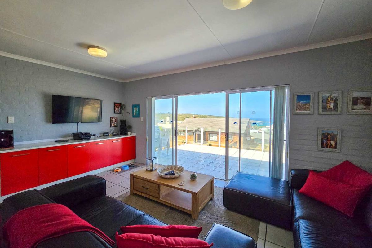 Spacious living room featuring built-in cabinetry, tiled flooring, and large sliding glass doors opening onto a tiled patio with coastal views.