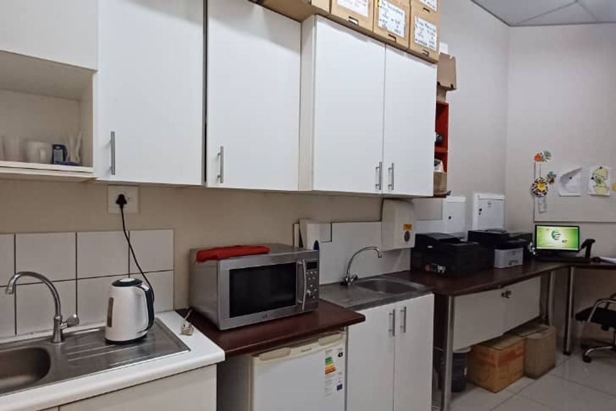 A functional kitchenette area featuring built-in cabinetry, a stainless steel sink, tiled splashback, and integrated counter space suitable for office or retail utility use.