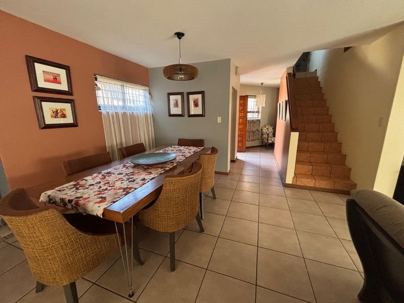 Dining area featuring tiled flooring, a staircase leading to the upper level, and a pendant light fixture, creating a functional open-plan living space.