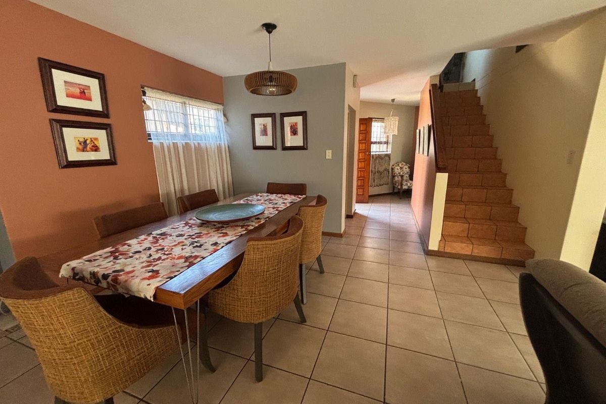 Dining area featuring tiled flooring, a staircase leading to the upper level, and a pendant light fixture, creating a functional open-plan living space.