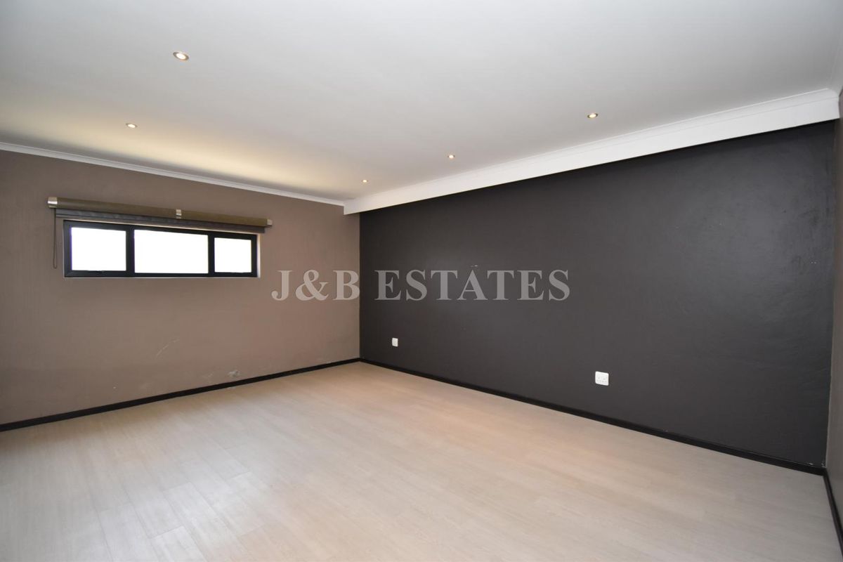 A spacious, empty bedroom featuring light-toned laminate flooring, recessed ceiling lighting, and a contrasting dark accent wall.