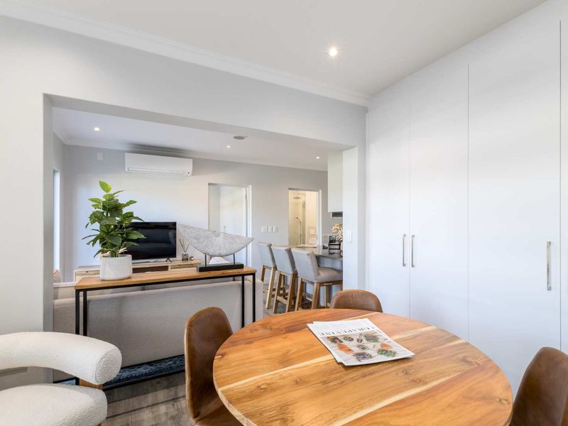 A bright open-plan living and dining area featuring modern downlights, a split system air conditioner, and extensive built-in storage cabinetry.