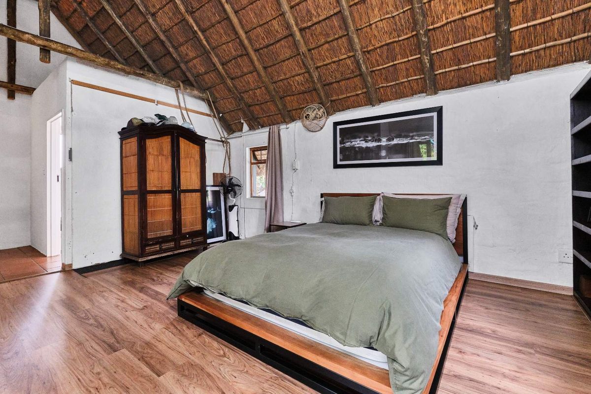 A rustic bedroom featuring a high vaulted thatched roof, exposed timber rafters, and wood-look flooring, creating a warm and character-filled living space.