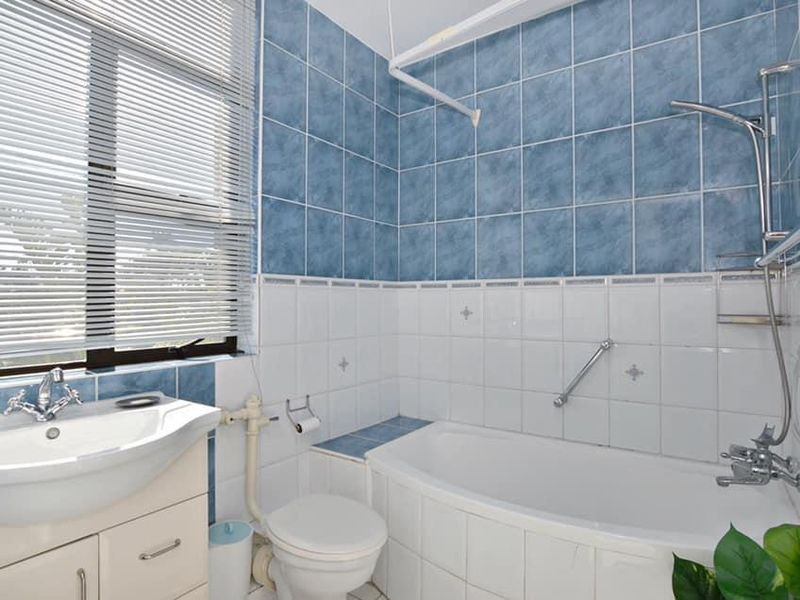 A functional bathroom featuring a vanity basin, bathtub with shower mixer, and tiled wall finishes with a window providing natural light.