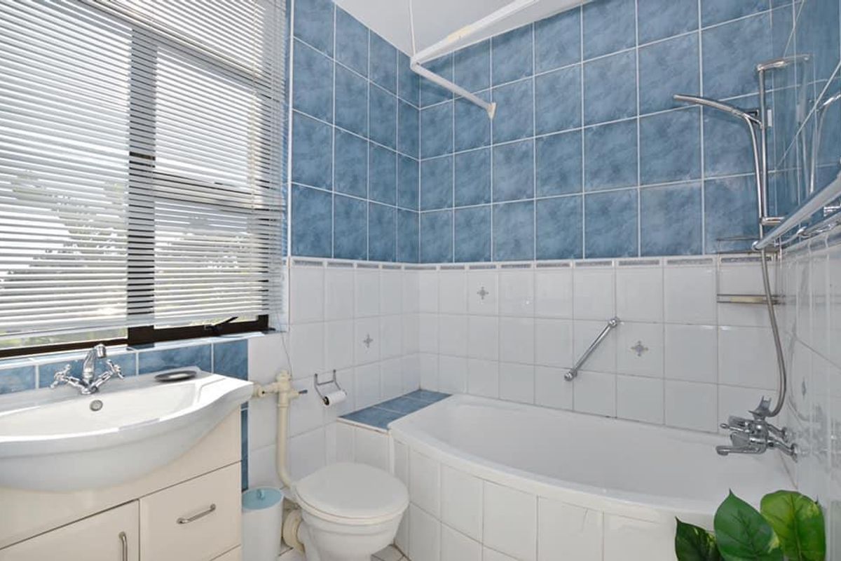 A functional bathroom featuring a vanity basin, bathtub with shower mixer, and tiled wall finishes with a window providing natural light.