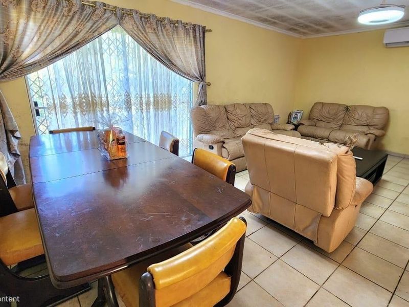 Open-plan living and dining area featuring tiled flooring, a wall-mounted air conditioner, and access to the exterior via a security gate.
