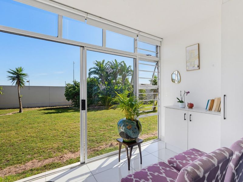Bright living area featuring large sliding glass doors that open onto a private garden, complemented by sleek tiled flooring and built-in storage cabinetry.