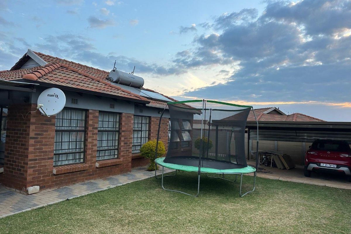 Rear view of a brick house featuring a tiled roof, solar geyser, and a paved area leading to a carport.