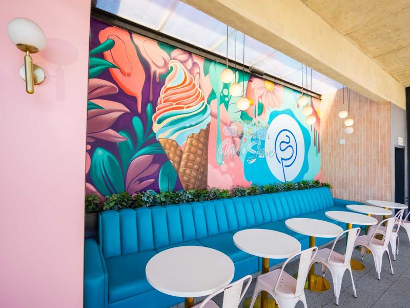 A vibrant, well-maintained outdoor seating area featuring a built-in blue bench, decorative wall mural, and modern pendant lighting.