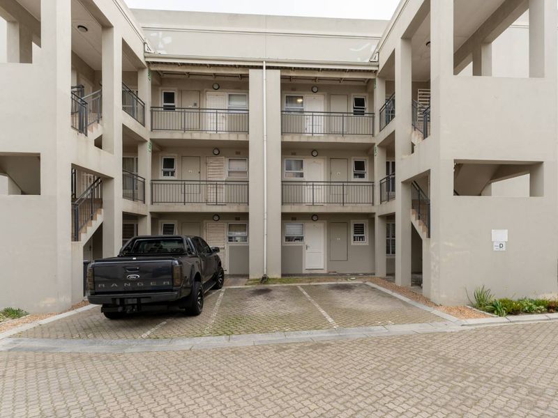 Front elevation of a multi-story apartment complex featuring paved parking bays, external staircases, and private balconies for each unit.