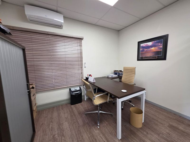 A functional office space featuring wood-look flooring, a suspended ceiling, and a wall-mounted split-system air conditioner.