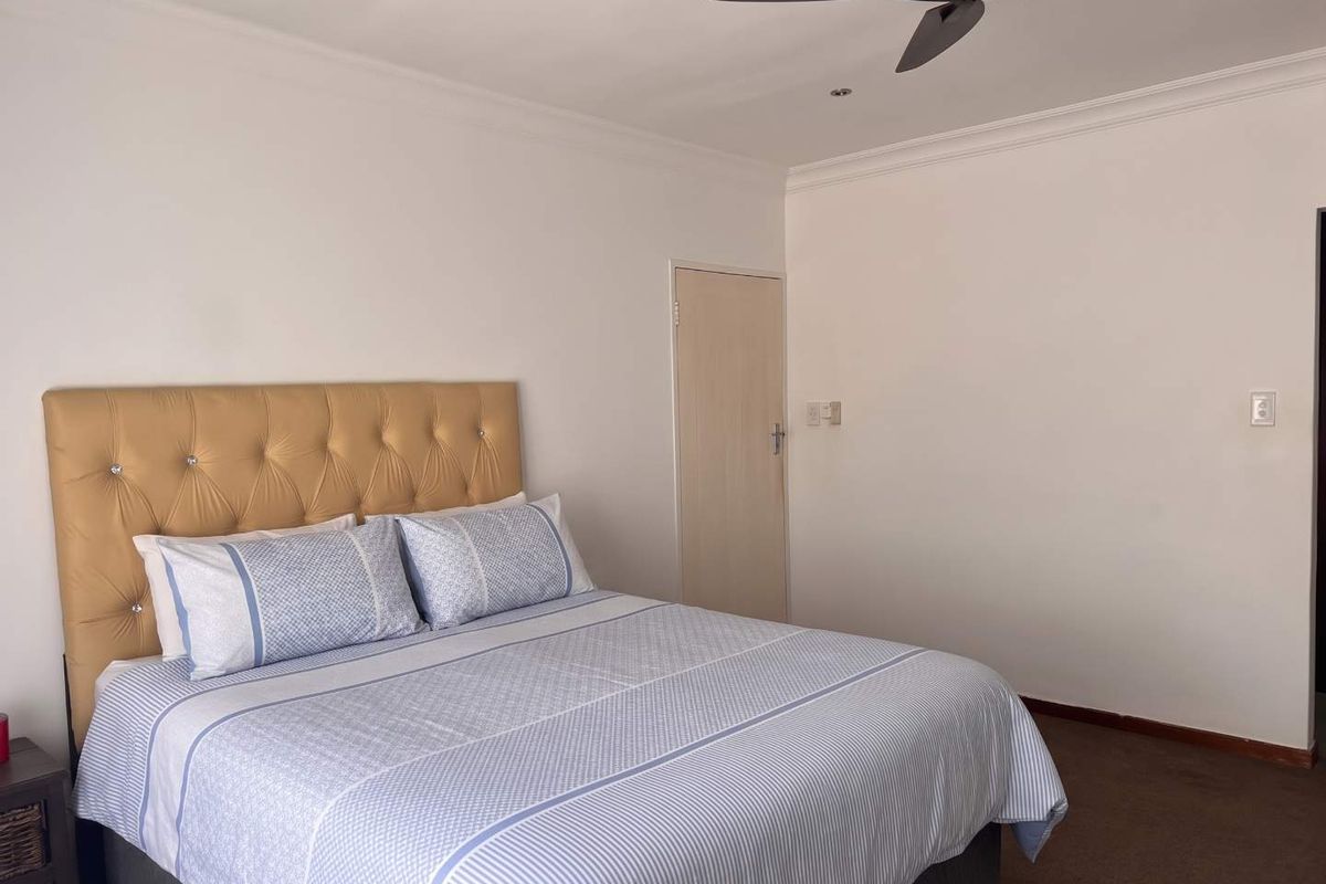 A simple bedroom featuring neutral walls, carpeted flooring, and a ceiling fan.