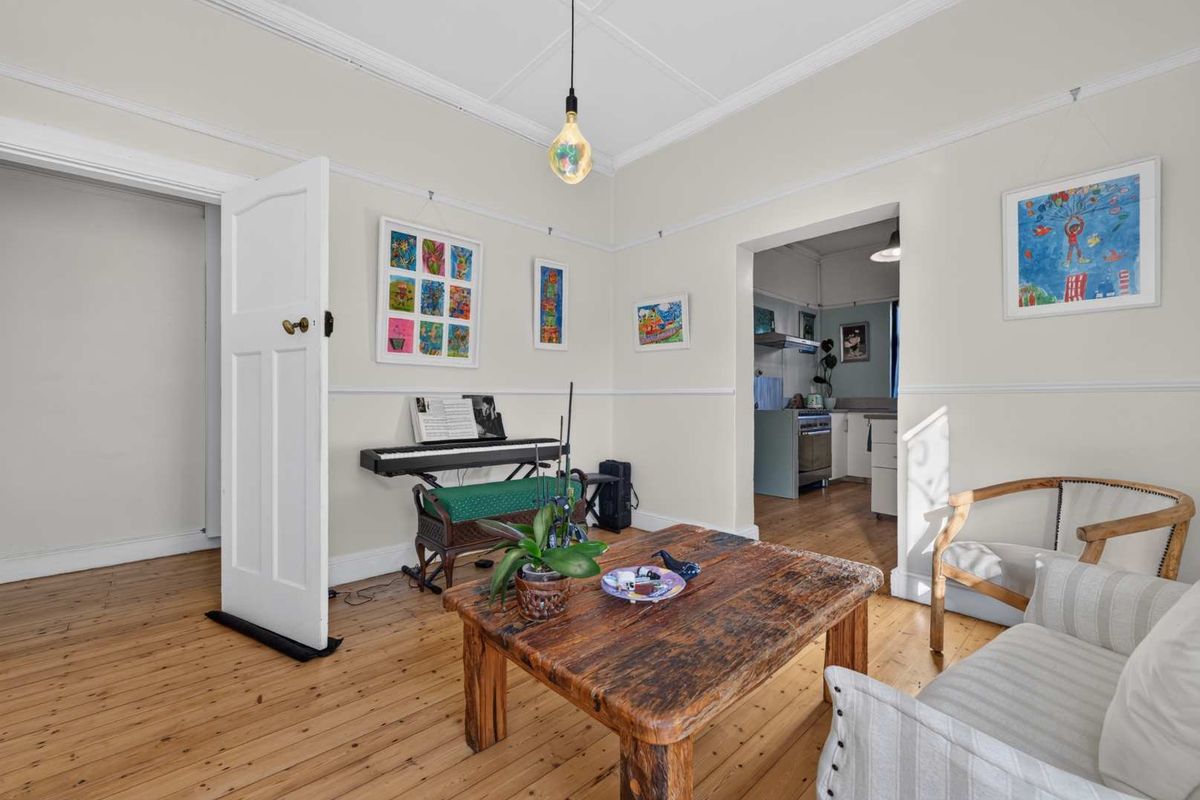 A bright living room featuring polished timber flooring, classic picture rails, and coved ceilings, with an open transition into the adjacent kitchen area.