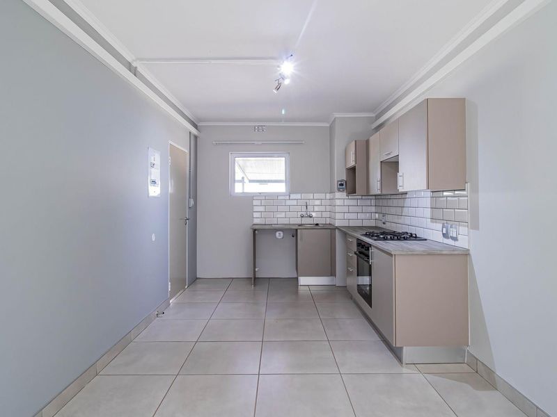 A clean, modern kitchen featuring neutral cabinetry, a gas hob, built-in oven, subway tile backsplash, and tiled flooring in an open-plan layout.