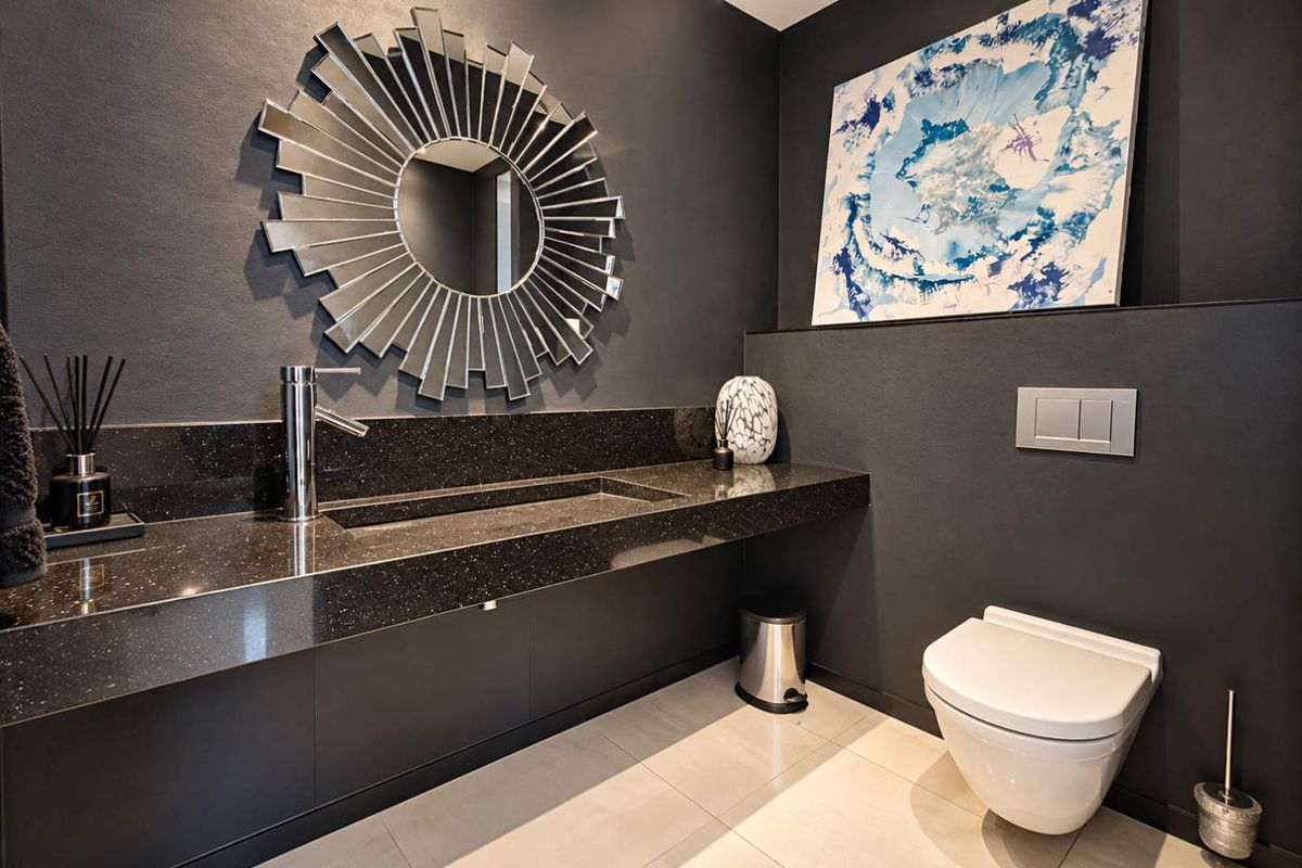 Modern guest bathroom featuring a sleek wall-mounted toilet, integrated stone vanity with recessed basin, and contemporary dark finishes.