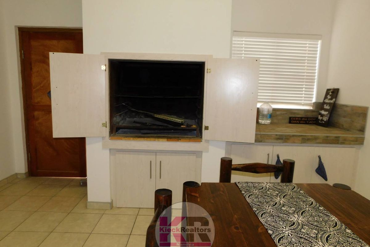 Indoor built-in braai area featuring cabinetry, tiled flooring, and a window with blinds, suitable for casual dining and entertaining.