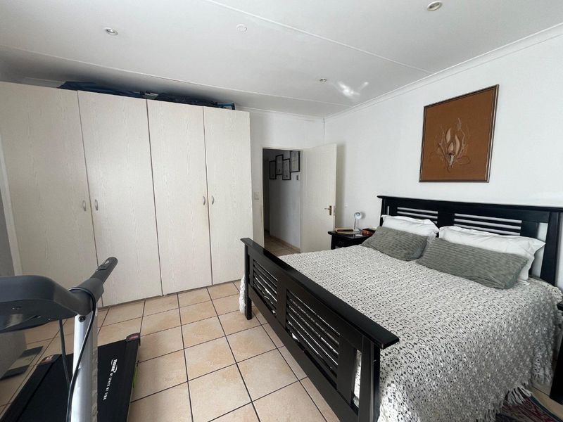 A functional bedroom featuring built-in cupboards, tiled flooring, and recessed downlighting, offering a practical layout for comfortable living.