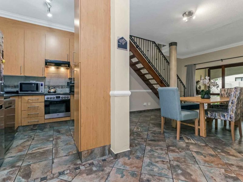 Open-plan kitchen and dining area featuring wood-finish cabinetry, tiled flooring, and a staircase leading to the upper level.