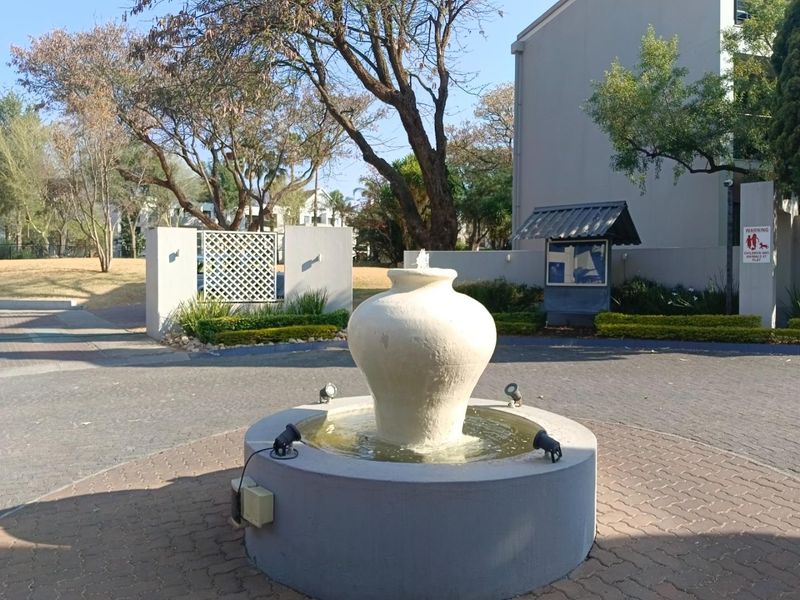 A well-maintained communal entrance area featuring a central water fountain, paved driveway, and landscaped perimeter walls within the apartment complex.
