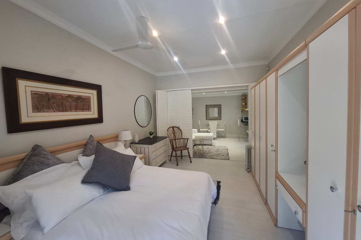 Spacious bedroom featuring built-in wardrobes, recessed ceiling lighting, and a ceiling fan, with an adjoining living area visible through double doors.
