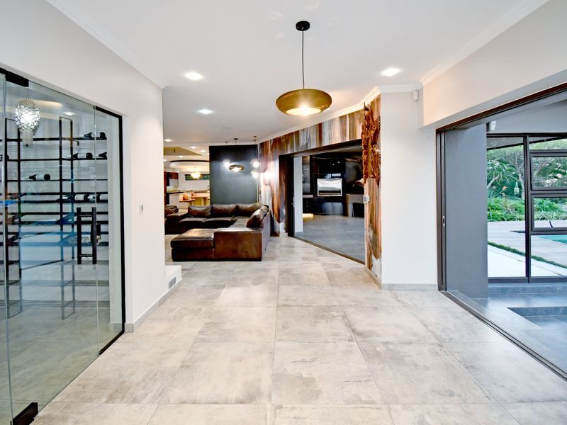 Spacious open-plan living area featuring large format floor tiles, recessed lighting, and a modern glass-enclosed wine cellar with seamless access to the outdoor pool area.