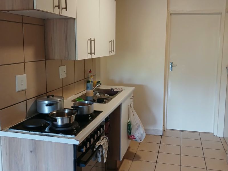 A functional kitchen featuring built-in cabinetry, a tiled backsplash, an electric hob with oven, and tiled flooring, with an unfinished ceiling.