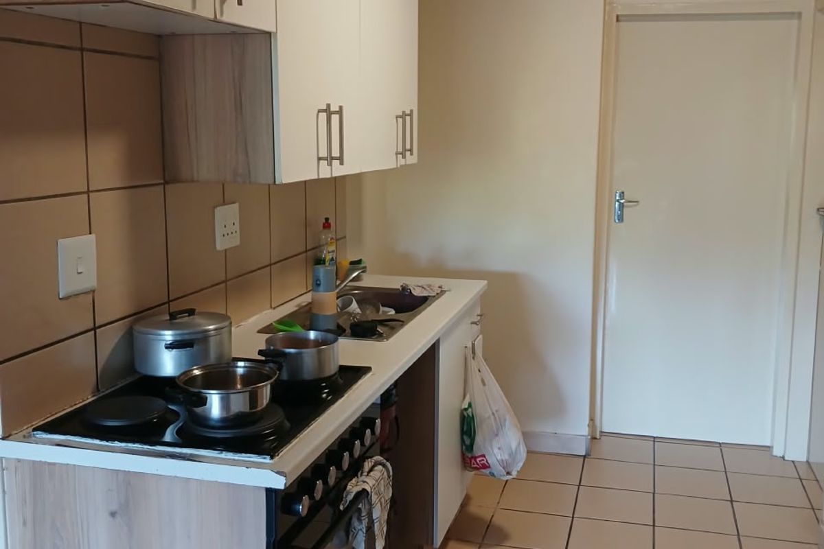 A functional kitchen featuring built-in cabinetry, a tiled backsplash, an electric hob with oven, and tiled flooring, with an unfinished ceiling.