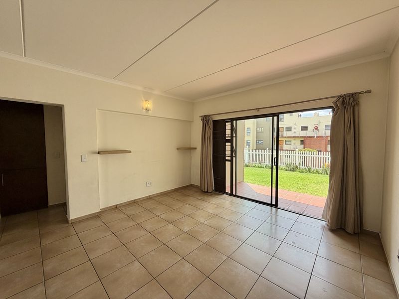 Spacious living area featuring neutral tiled flooring and a large sliding glass door providing direct access to the patio and garden.